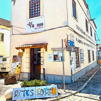 Painting of a corner building in Melides, Portugal, with cobblestone streets, cream-colored walls, and signs for a cultural and artisan space. A colorful handmade “Artesanato” sign and posters adorn the entrance under a small tiled awning. The following images show the same artwork displayed in different interior settings.