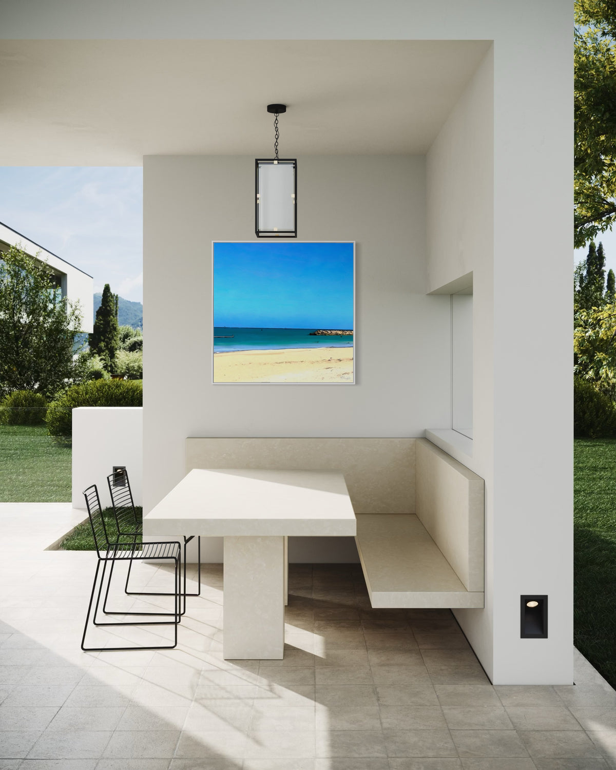 Modern outdoor dining nook with built-in cream seating, a minimalist table, and black wire chairs. Rosalie Powell’s Perfect Water artwork adds a vibrant coastal touch, depicting golden sand and turquoise sea under a vivid blue sky. Surrounded by lush greenery and clean architectural lines, the space feels serene and contemporary.