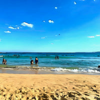 Painting of Bondi Beach in the late afternoon, with soft waves, golden sand, and beachgoers wading in the water under a clear blue sky. The following images show the same artwork displayed in different interior settings.